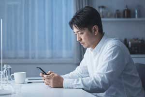 妻が隣にいても会話をせず、スマートフォンを無表情で見つめる日本人男性。心の交流が起きにくい夫婦の会話パターンやすれ違いの日常風景。。